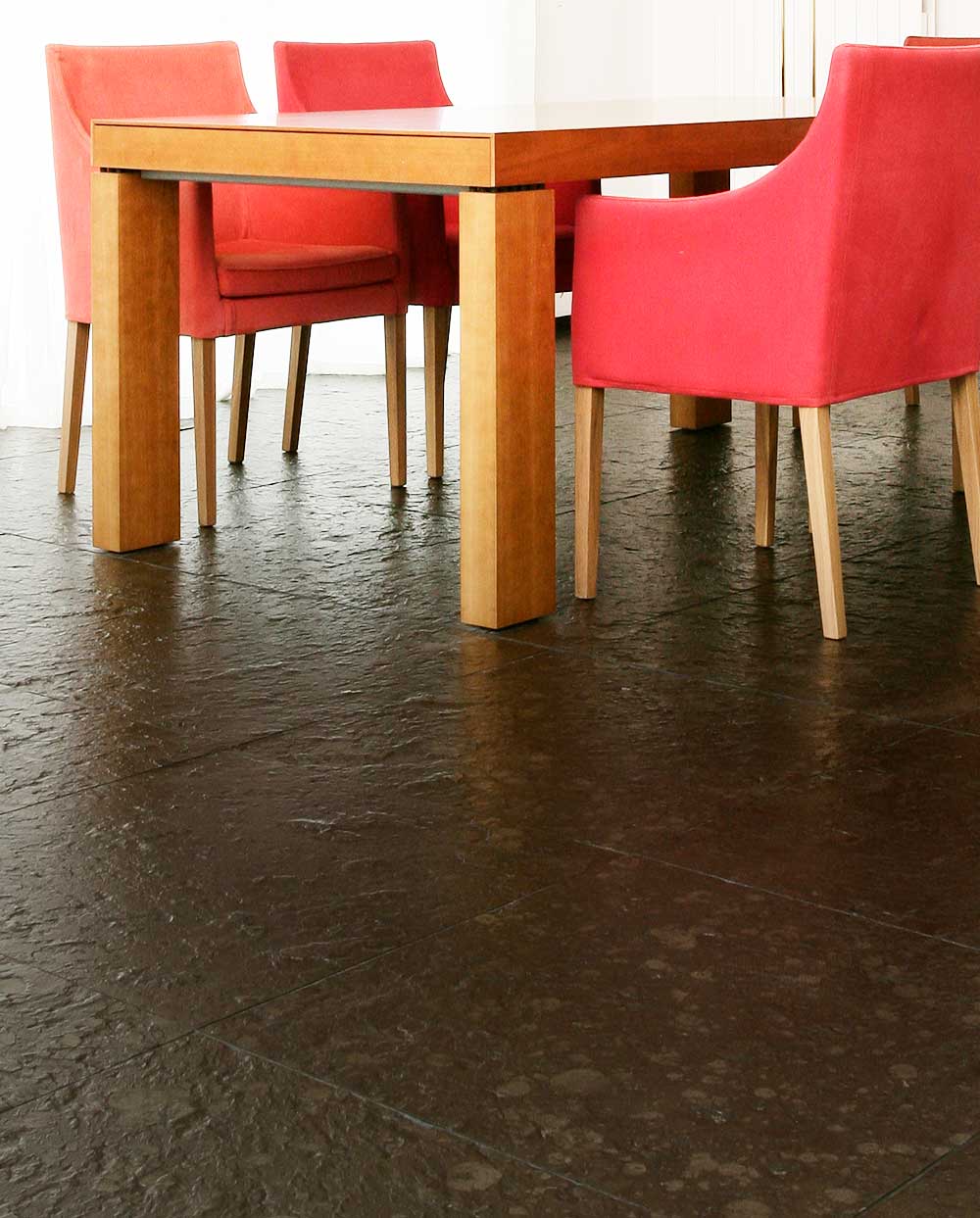 Holztisch mit roten Stühlen auf quadratischen Schieferfliesen